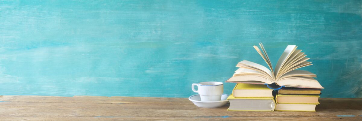 Stack of books with an open book and a coffee cup on a wooden table, symbolizing resources and books for aspiring investors