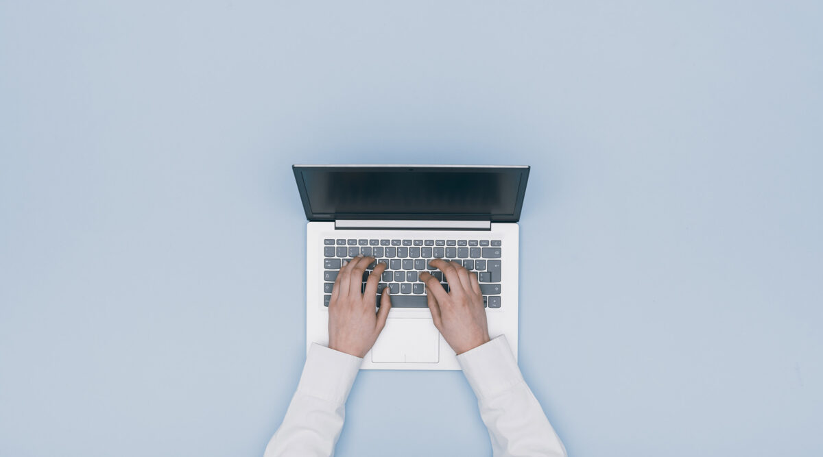 Top view of hands typing on a laptop, representing virtual employee onboarding during remote work.