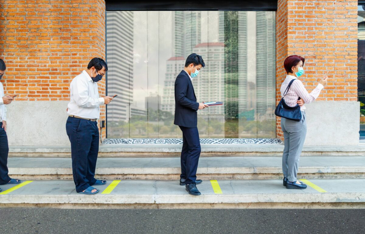 People wearing masks standing in a socially distanced line, reflecting new norms and behaviors during the COVID-19 pandemic.